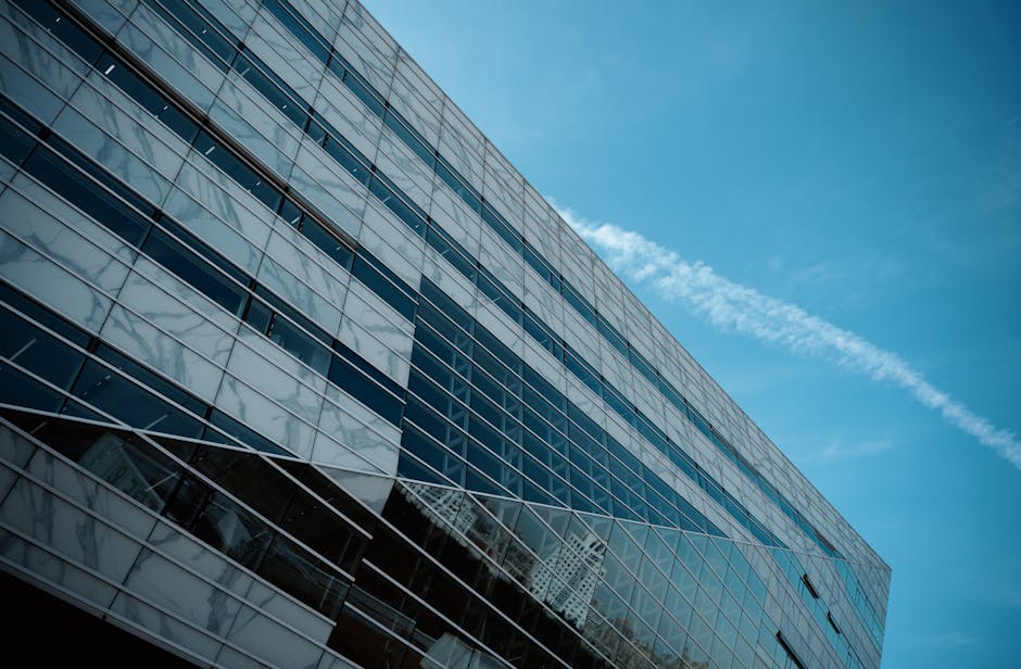 A striking low angle view of a modern glass building against a clear blue sky